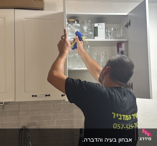 אדם מבצע הדברה בארון מטבח עם כלי עבודה.